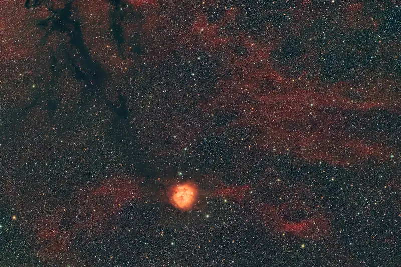 The Cocoon Nebula, a red emission nebula at the end of a long dark dust lane